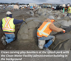 Crews carving play boulders at the splash park with the Clean Water Facility administration building in the background