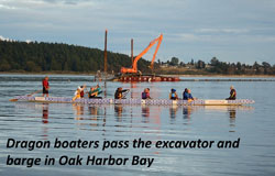 Dragon boaters pass the excavator and barge in Oak Harbor Bay